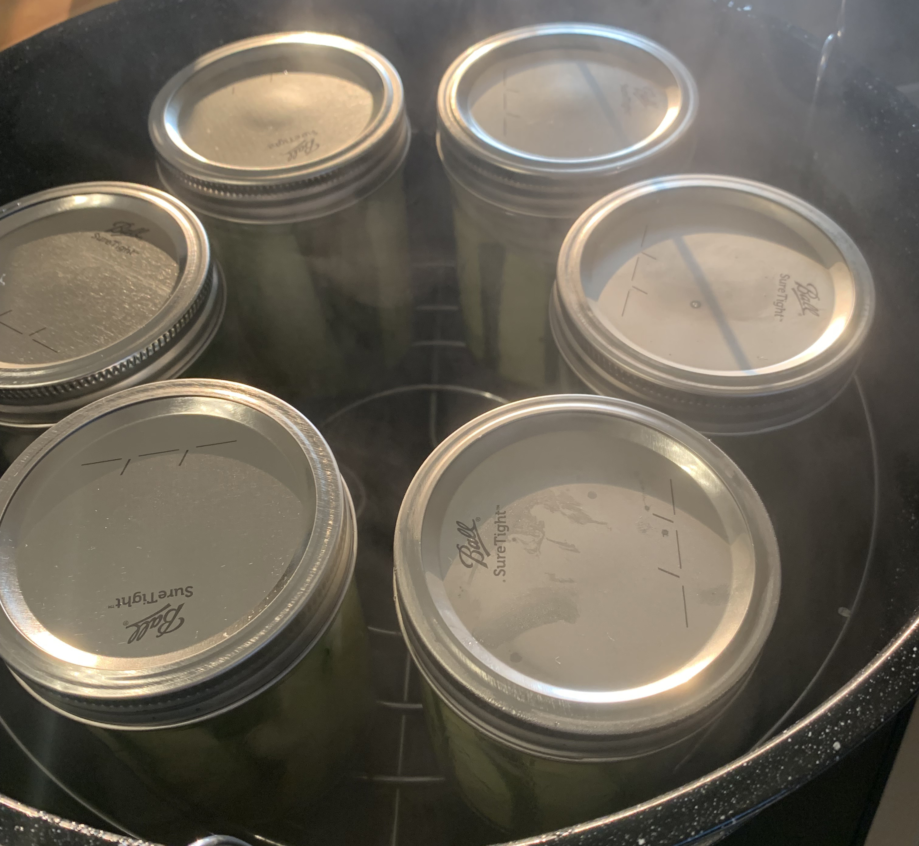 six mason jars about to be submerged in a large pot of boiling water