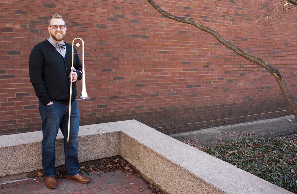 a man stands in front a brick wall holding a trombone